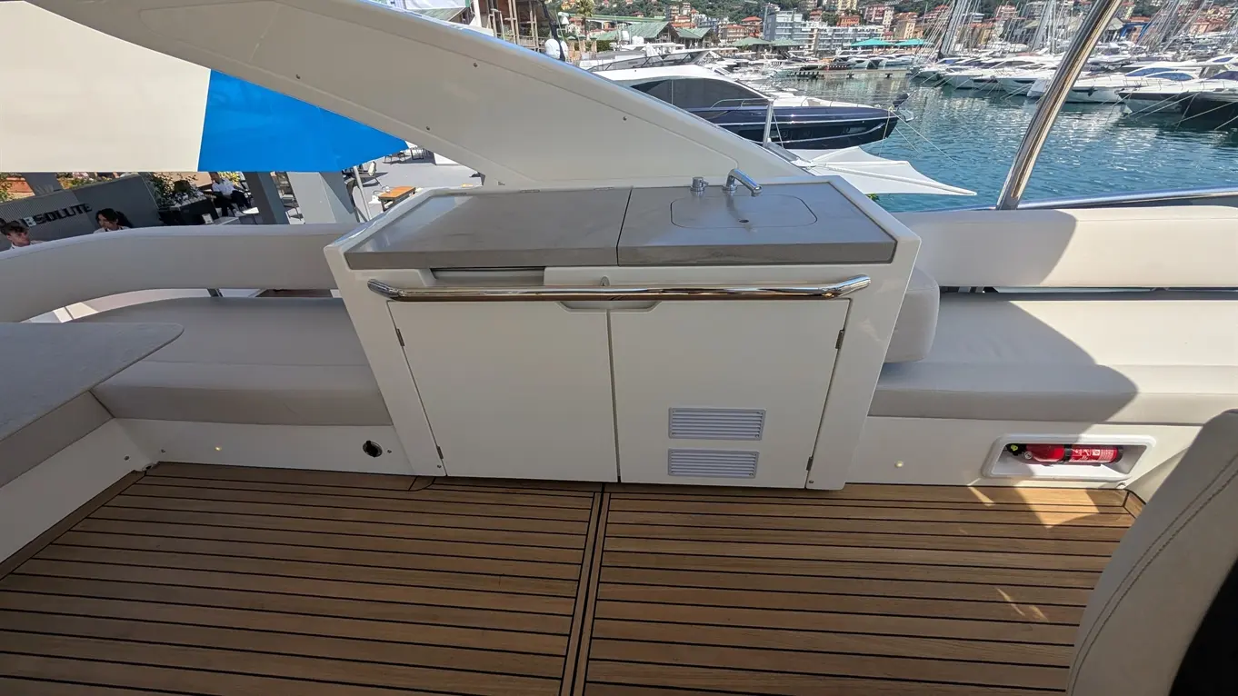 A luxury yacht's outdoor kitchen area features a sink, storage unit, and wooden deck, with boats visible in the background.